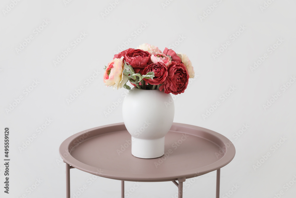 Vase with bouquet of beautiful flowers on stylish table near light wall