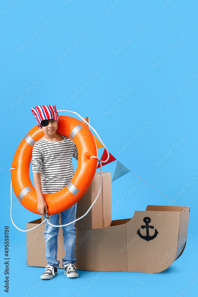 Cute little boy playing with cardboard ship on blue background