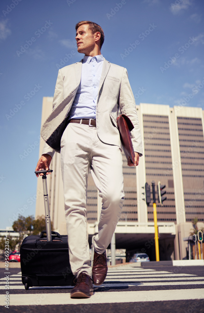 All work no play. Shot of a young businessman walking with a suitcase in the city.