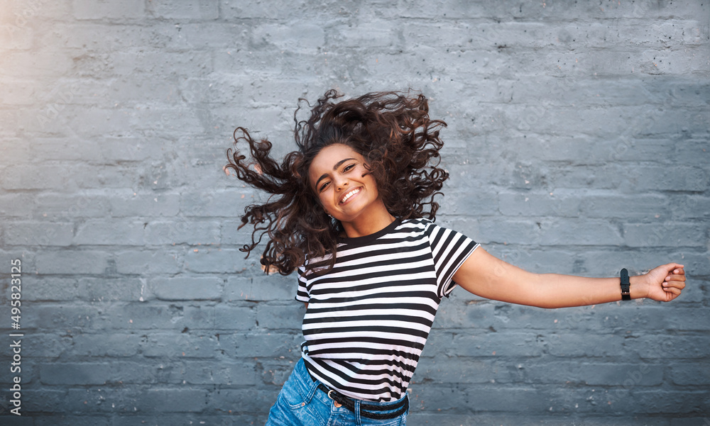 Dancing is one shortcut to happiness. Portrait of a young woman dancing against a grey wall.