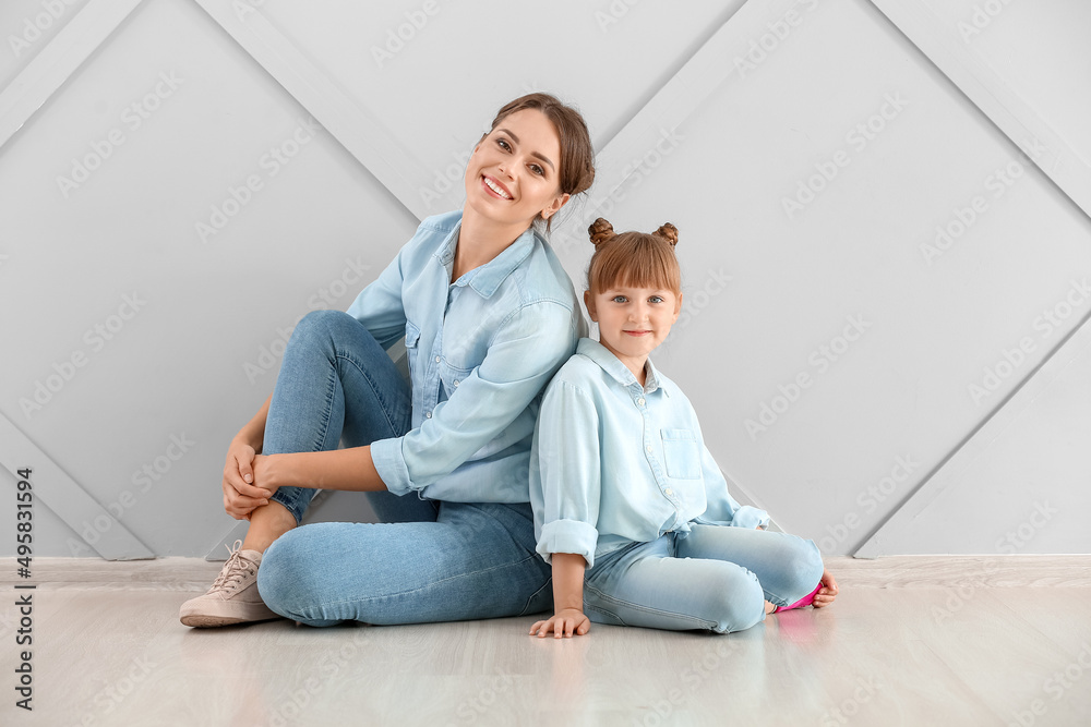 Portrait of happy mother and daughter sitting on floor near wall