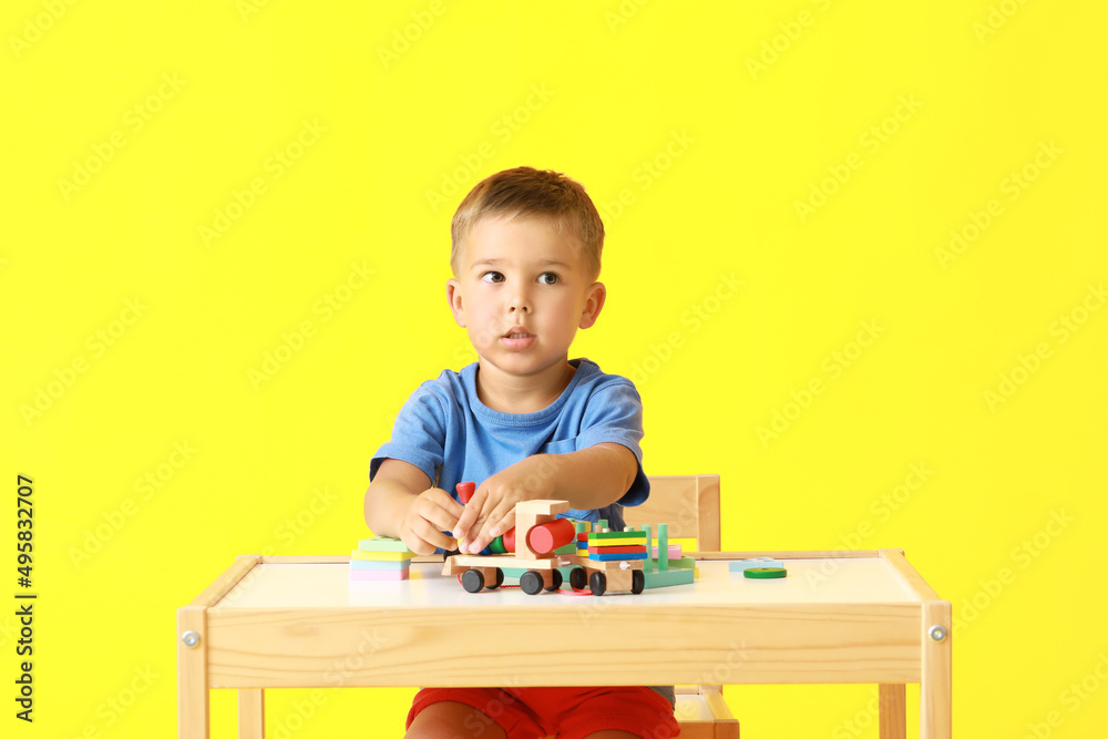 Cute little boy playing with building blocks at table on yellow background