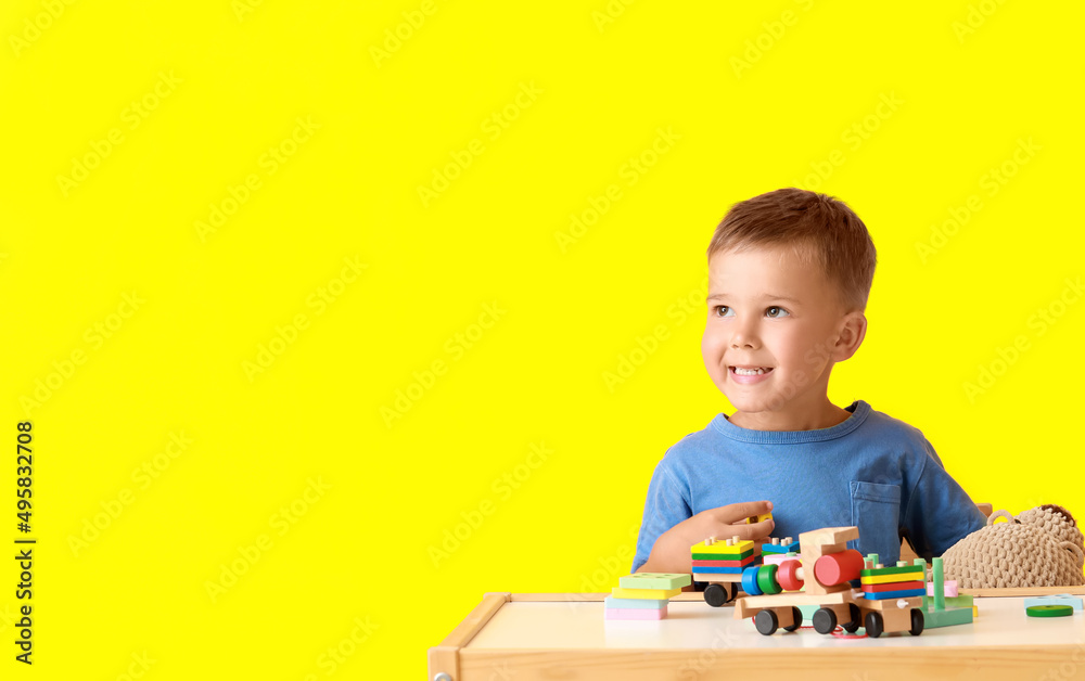 Cute little boy playing with building blocks at table on yellow background