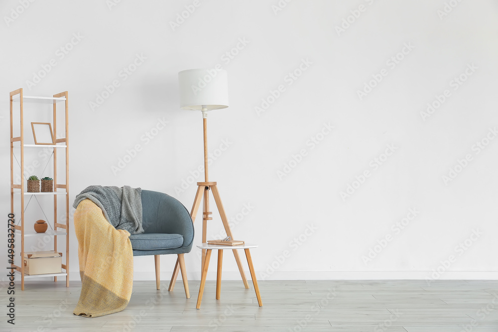 Grey armchair with plaid, table and shelving unit near light wall