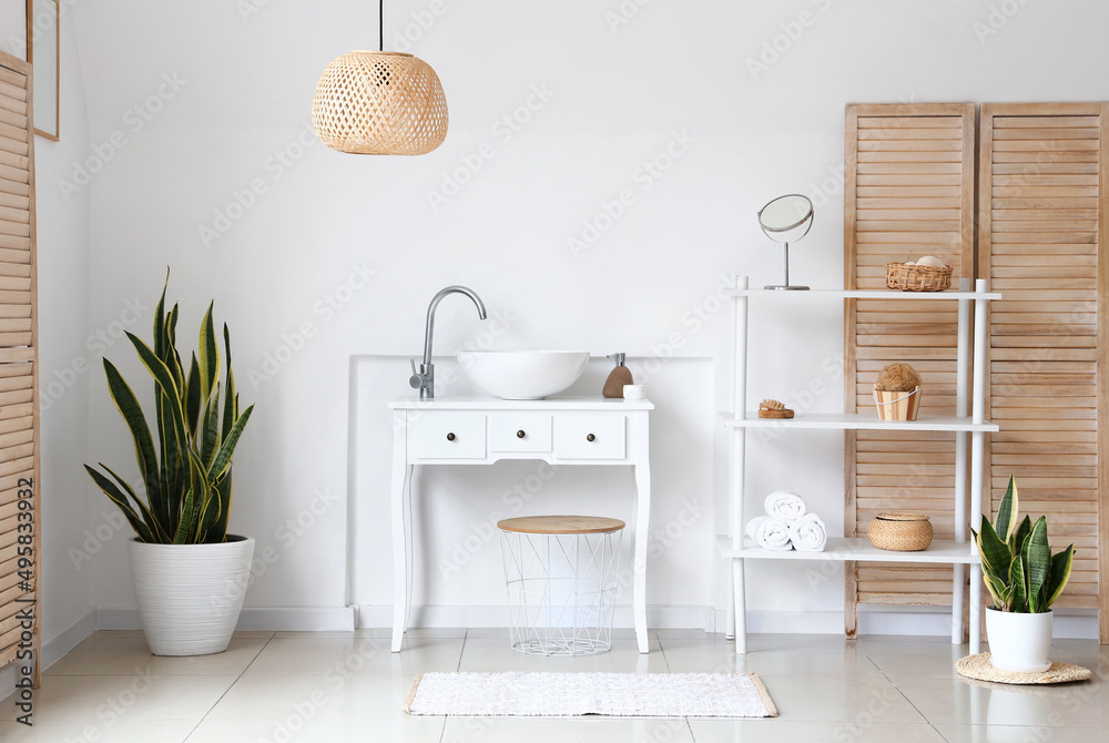 Interior of light bathroom with sink, shelving unit and houseplants