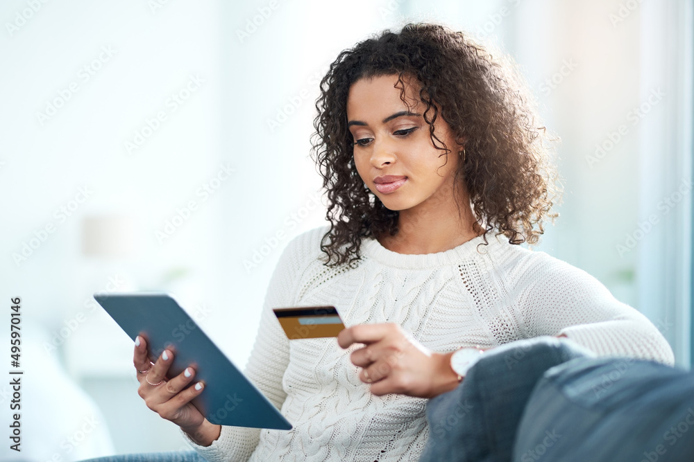 Make smarter purchases. Shot of a young woman holding her credit card while using a digital tablet.