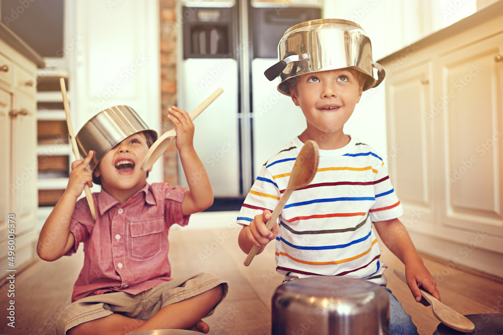 Lets get this party started. Two young boys sitting on the kitchen floor playing with pots and pans.