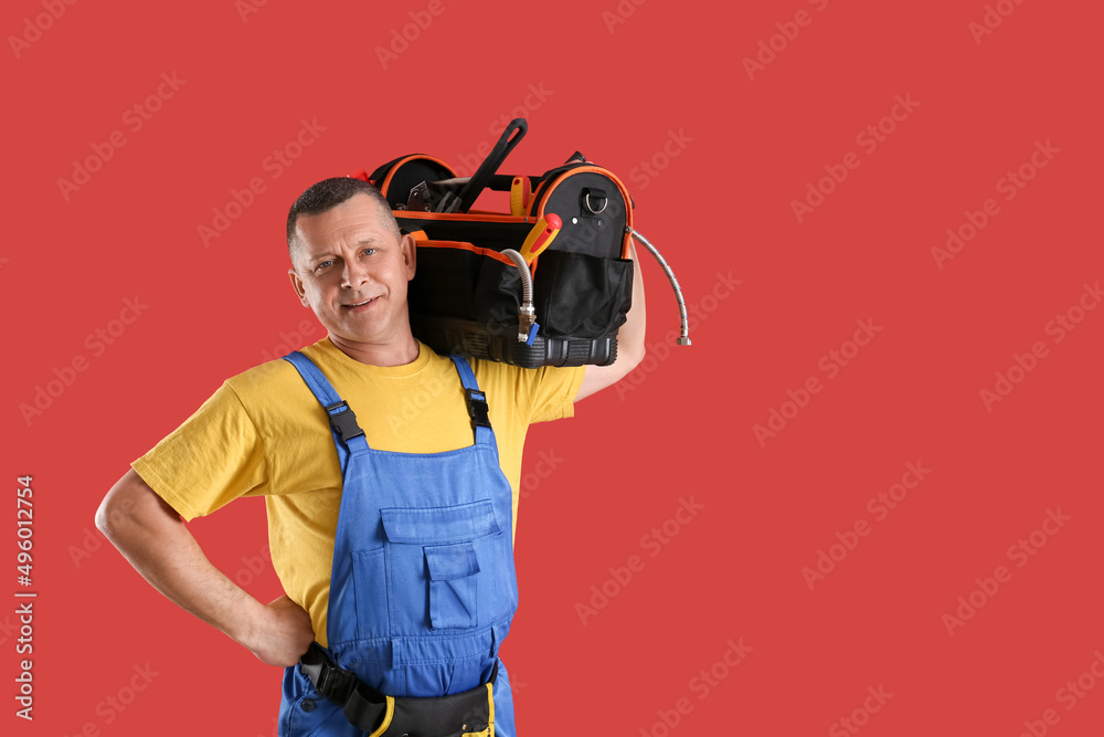 Handsome plumber with tools bag on color background