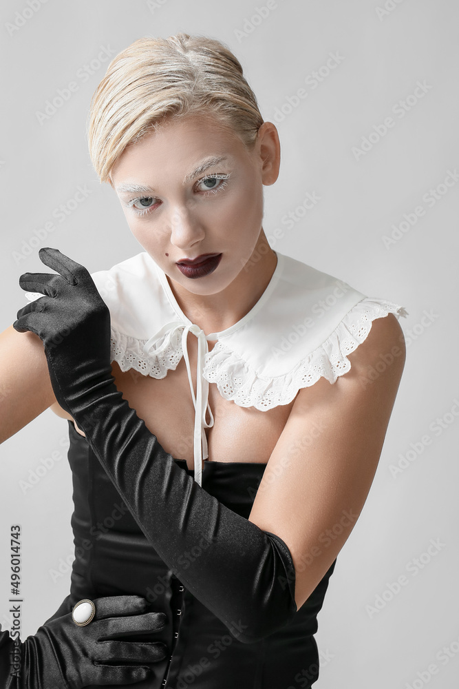 Beautiful young woman with creative makeup and elegant gloves on grey background