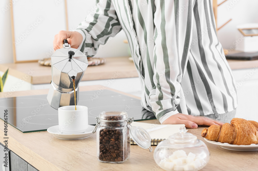 Young woman pouring coffee into cup in kitchen