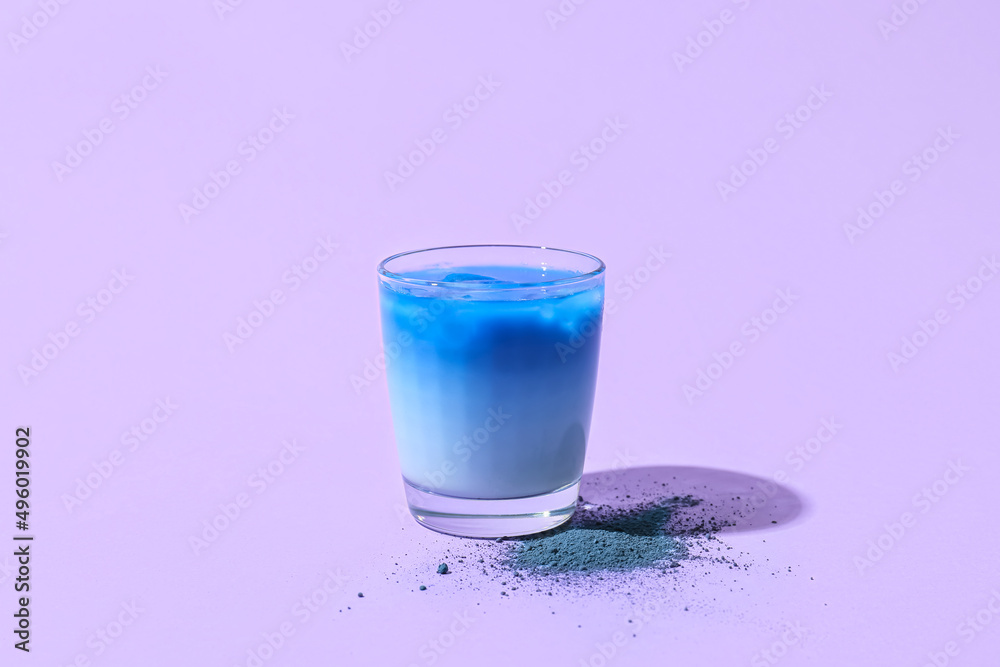 Glass of blue matcha tea and powder on purple background