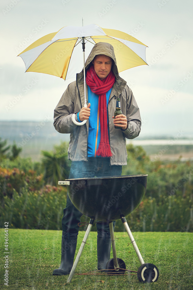 Real men bbq anytime. Shot of a man barbecuing in the rain.