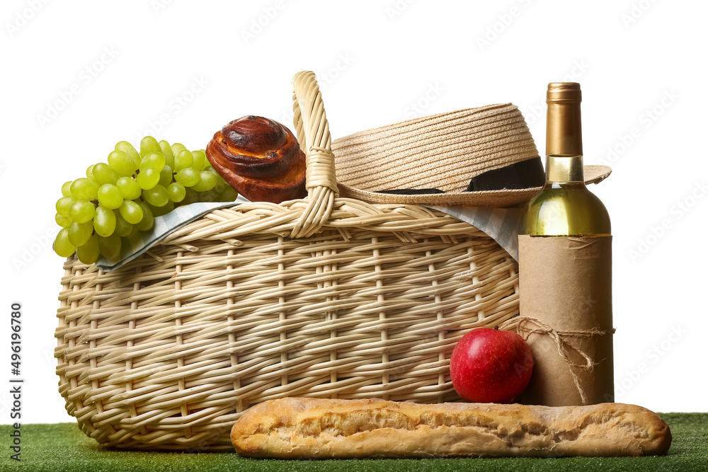 Wicker basket with tasty food and wine for picnic with hat on white background