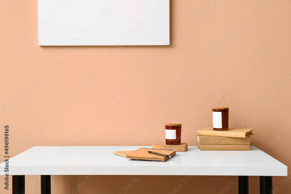 Notebooks, books and candles on table near color wall