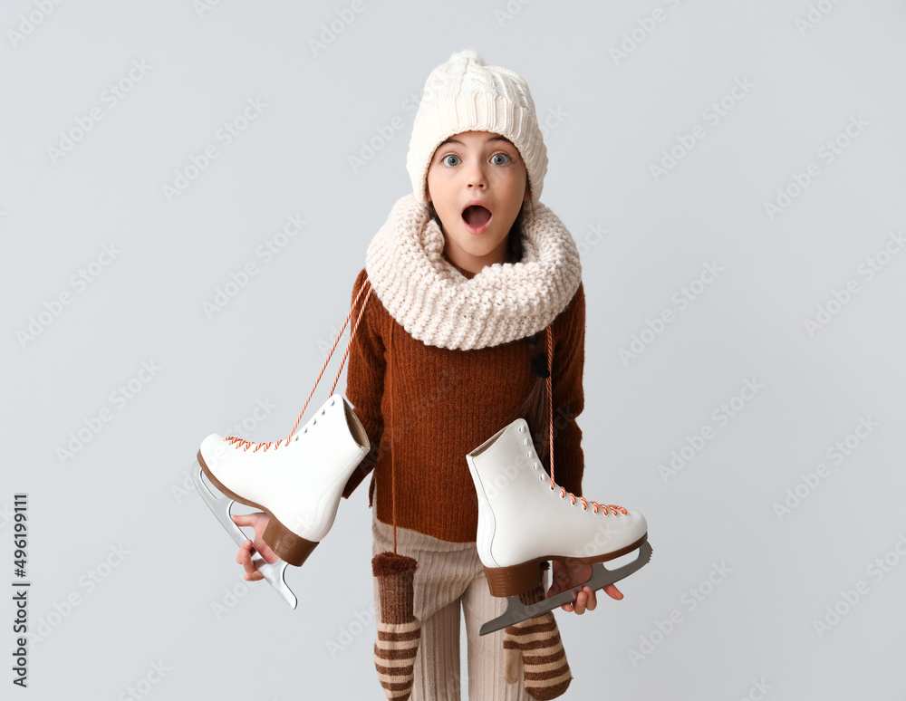 Surprised little girl with ice skates on grey background