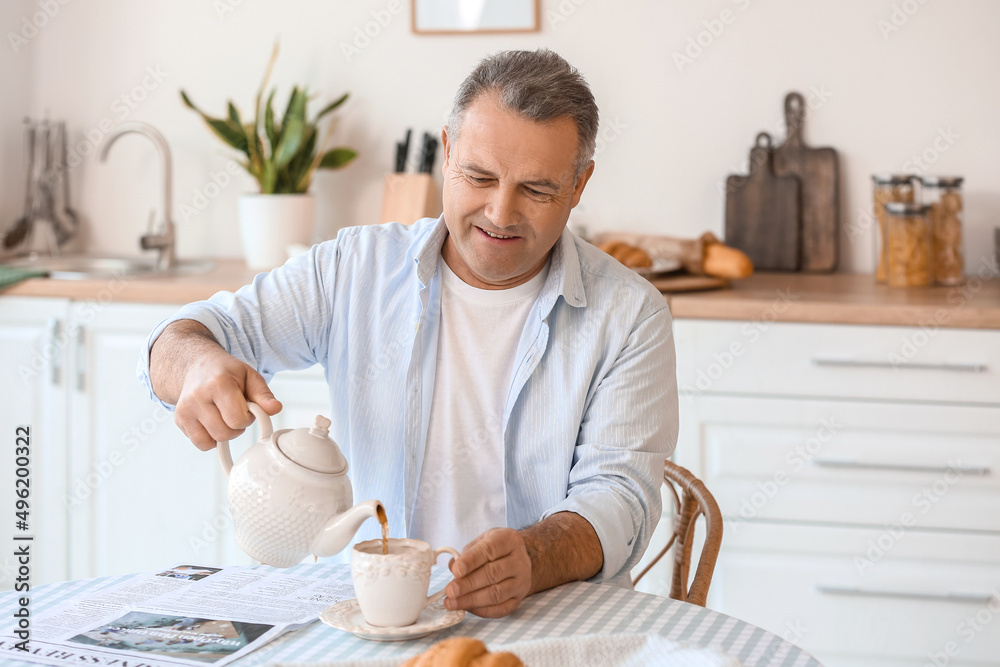 厨房餐桌上的一位老人正在往杯子里倒茶