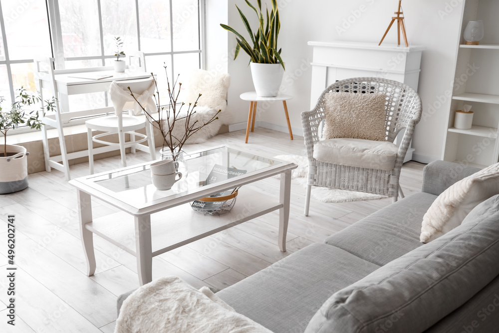 Table with cups, armchair and sofa in light living room interior