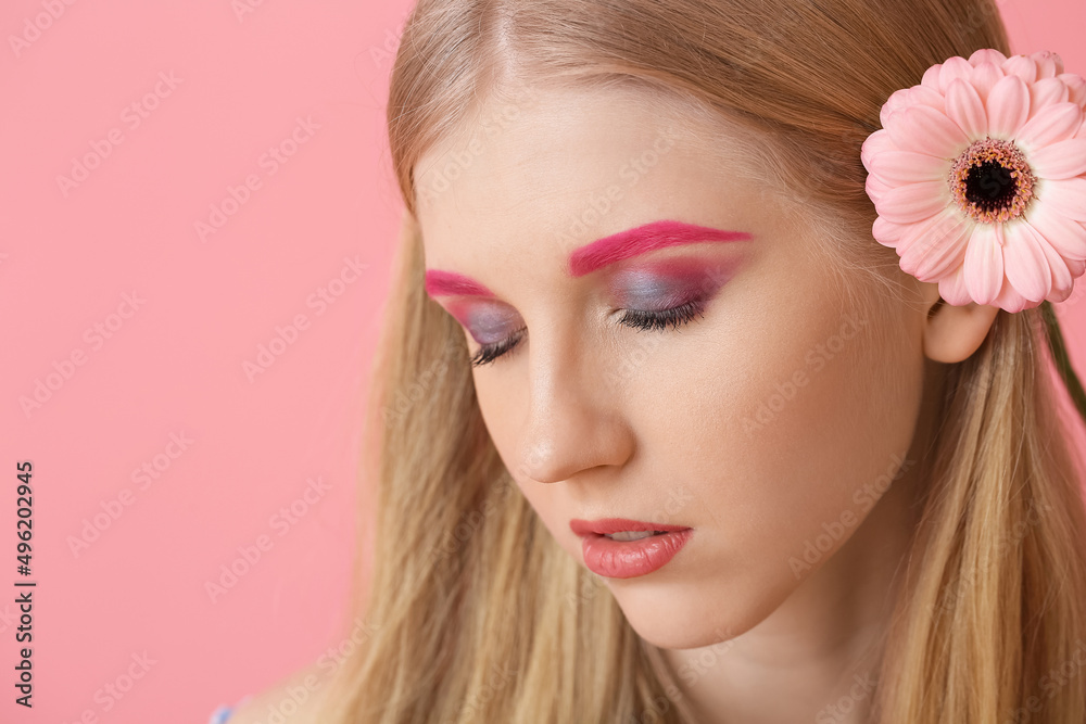 Young woman with creative makeup and gerbera flower on color background