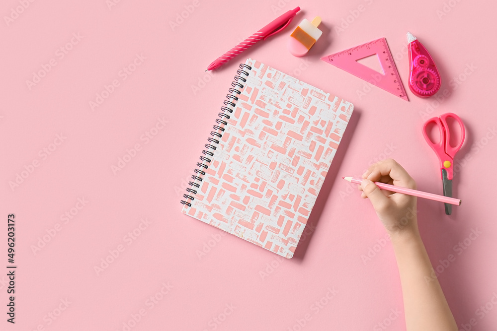 Childs hand with different stationery on pink background