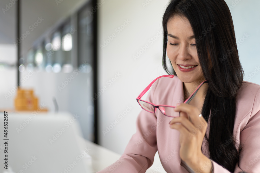 Asian businesswoman working on laptop in office holding glasses and has blurry vision, tired from lo