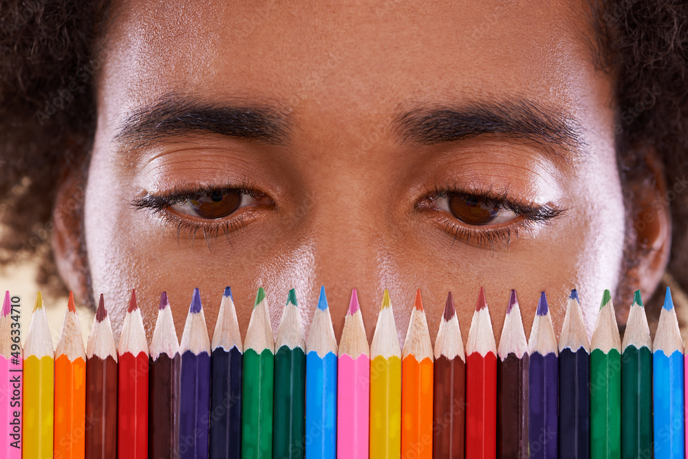 Hmm, so many colors.... Cropped view of an african man looking closely at a row of colorful pencil c