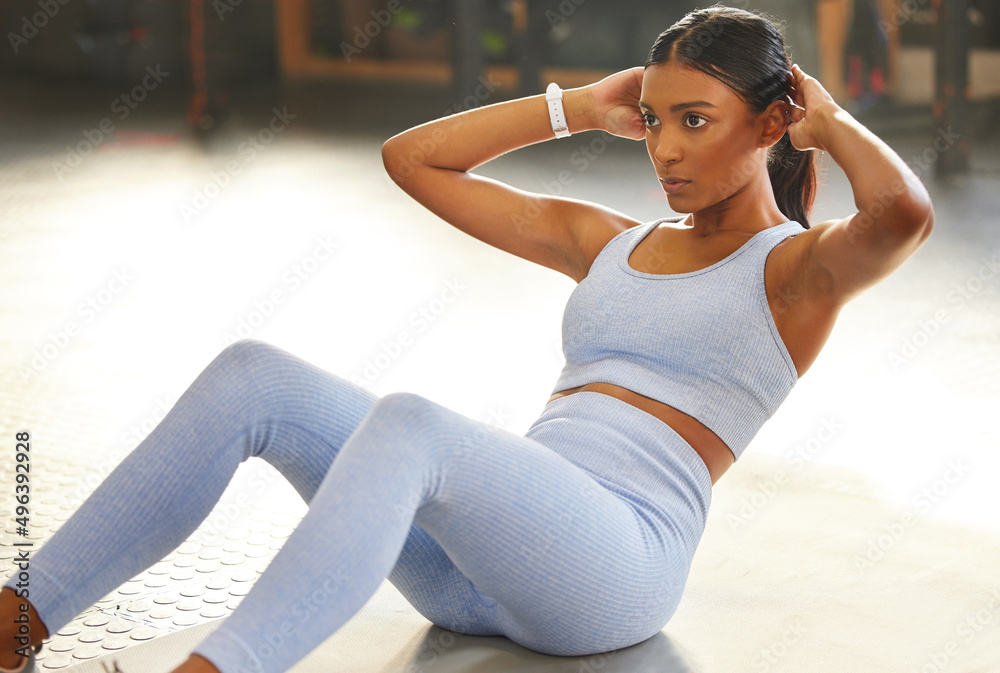 Rock hard abs take real dedication. Shot of a fit young woman doing sit ups in a gym.