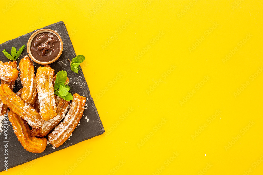 Plate with fried churros and chocolate sauce, top view