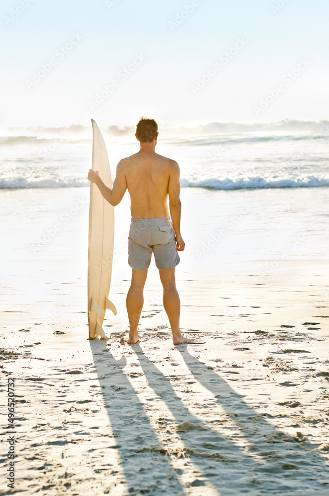 Ive never seen a more beautiful view. Rearview shot of a muscular young man holdng his surfboard whi