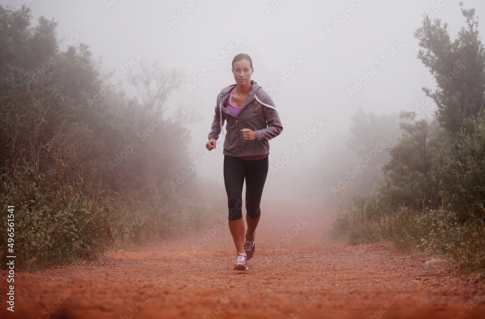 Shes committed to staying in shape. Shot of a woman running on a trail on a misty morning.