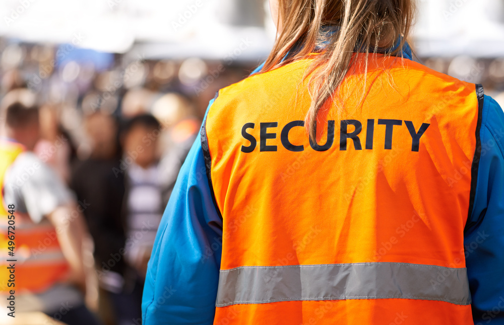 Safety is the main aim. Rearview shot of a security officer standing outdoors with a crowd in the ba