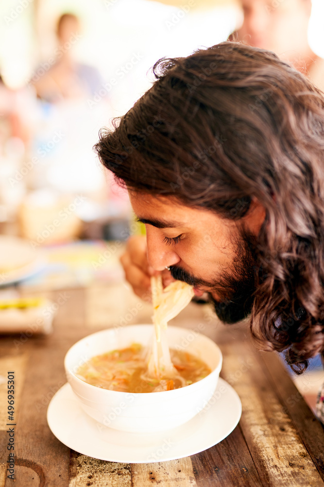 Enjoying a bowl full of noodles. Shot of a young man eating a bowl of noodles in a restaurant in Tha