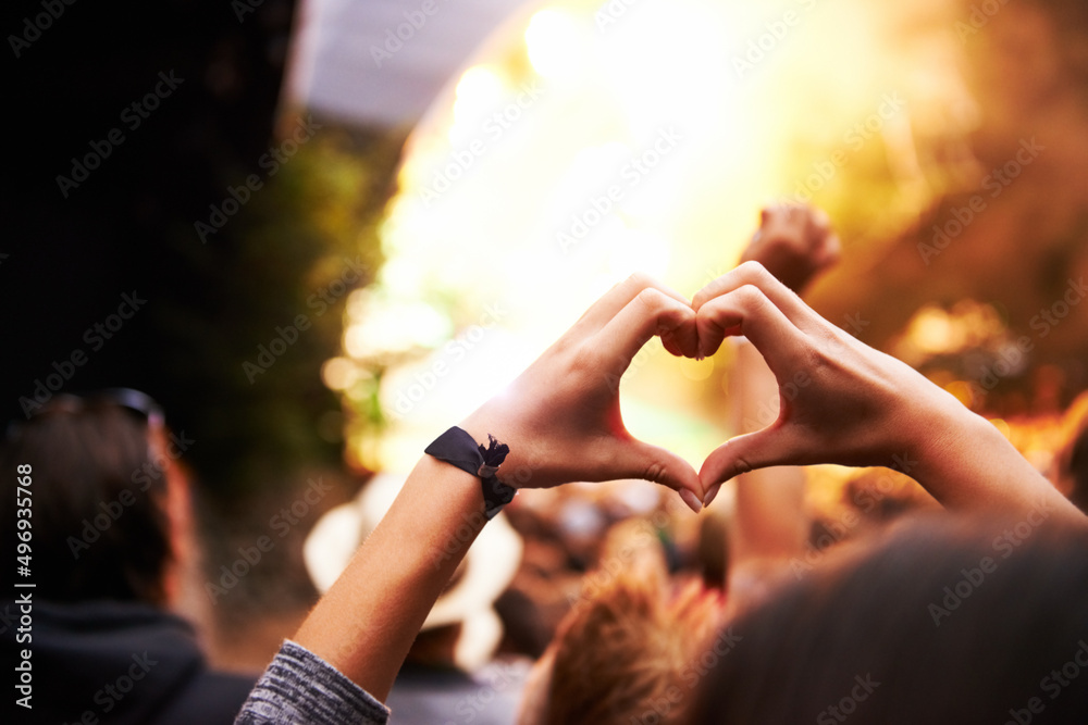 Appreciating the art of performance. A young woman gesturing a heart towards the stage at a music fe