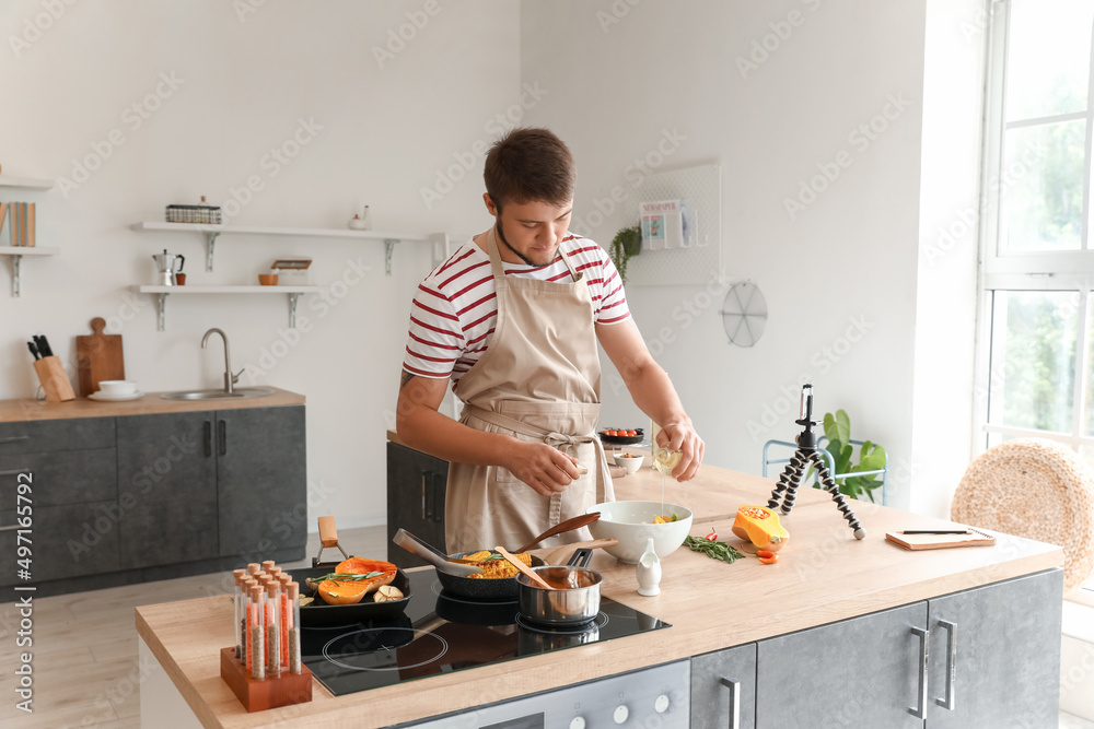 Young man pouring oil into bowl with salad in kitchen