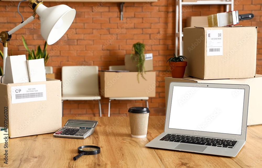 Cardboard boxes with belongings and laptop on table in office on moving day