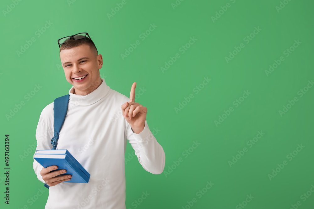 Male student with books pointing at something on green background