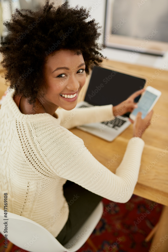 Making plans for the weekend. Portrait of an attractive young using her cellphone and laptop at home