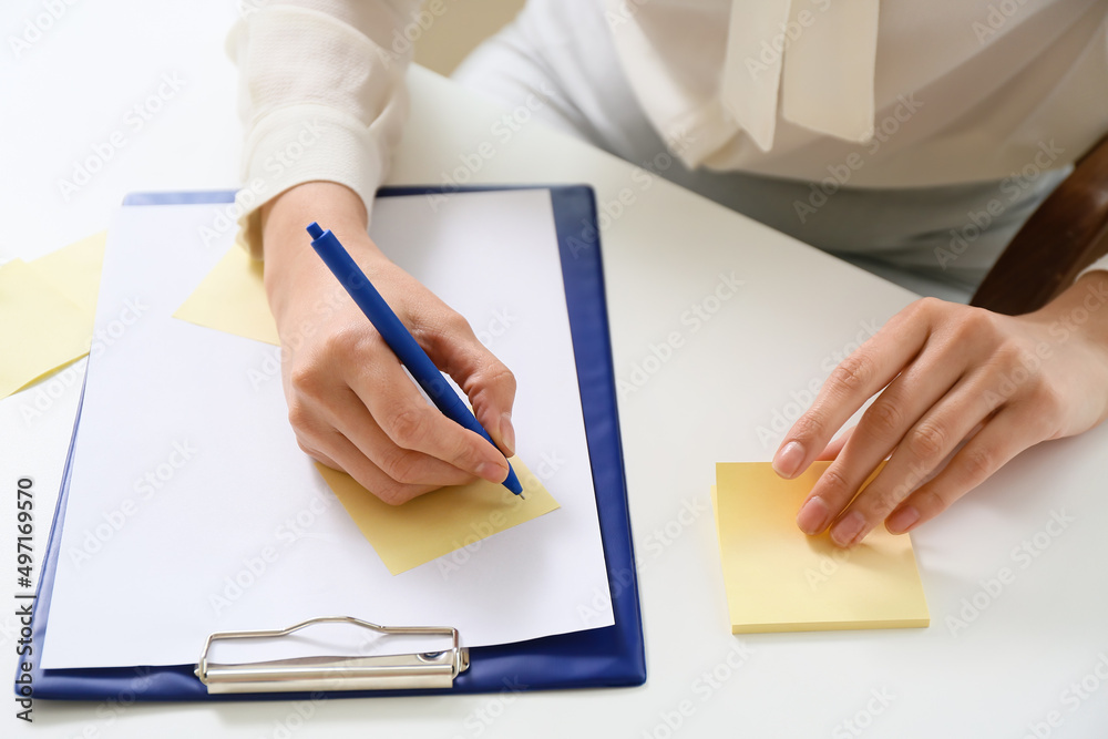 Young manager writing on sticky note paper in office, closeup