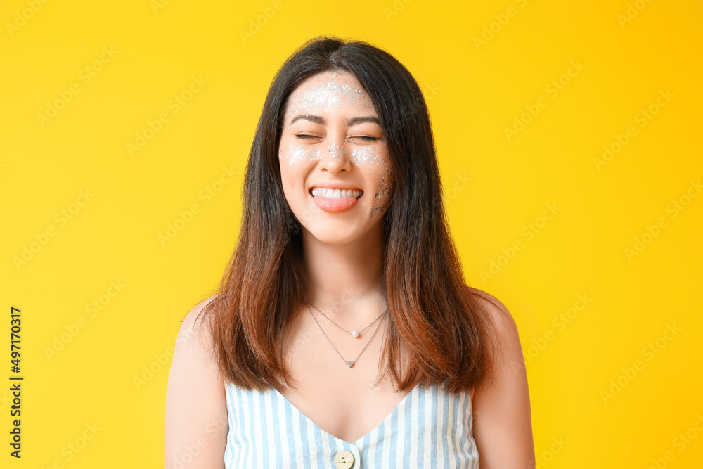 Happy Asian woman with glitter makeup and closed eyes on color background