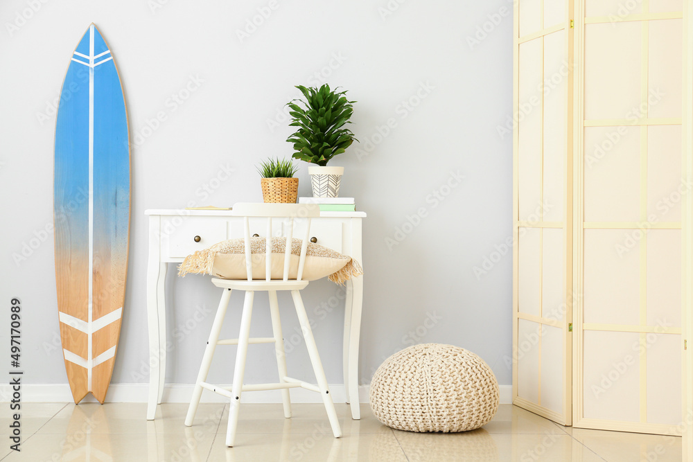 Workplace with houseplants and surfboard near light wall