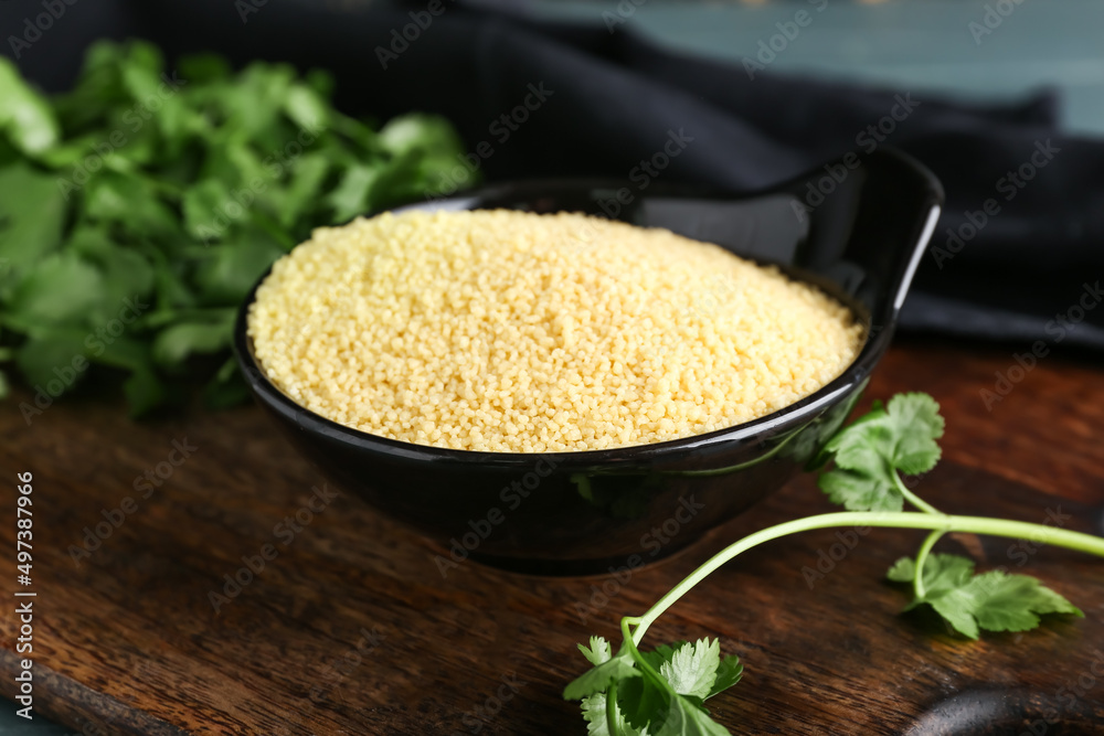 Bowl of raw couscous with parsley on table