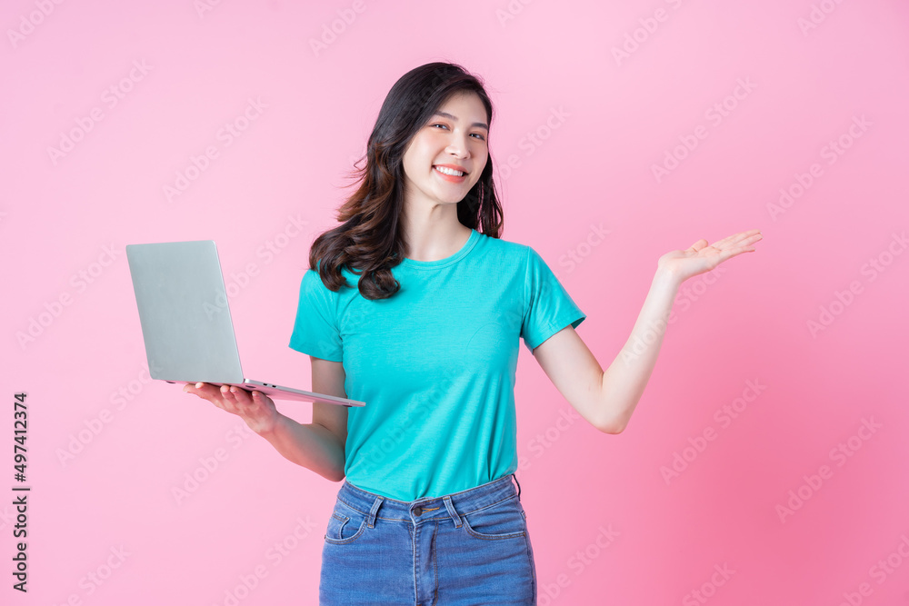 Young Asian woman using laptop on pink background