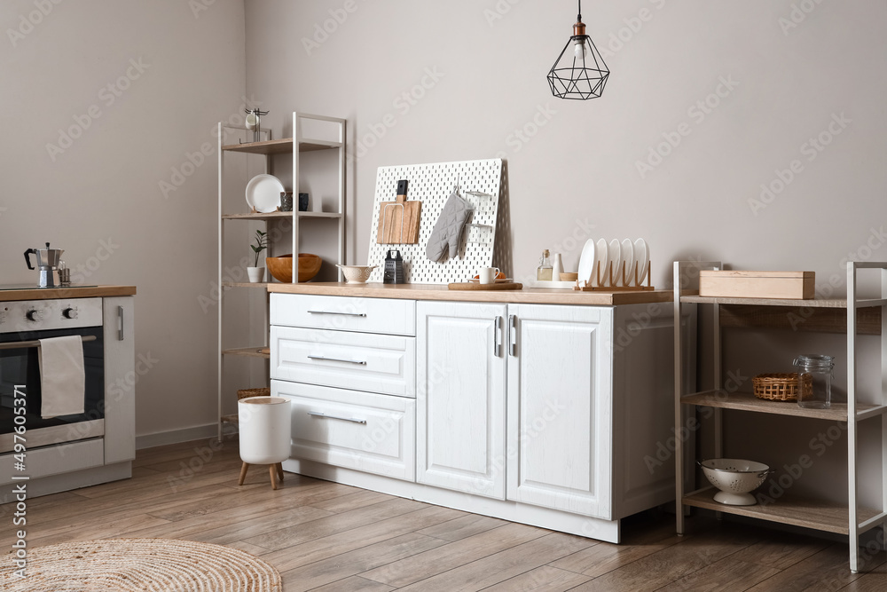 Modern shelving unit with dishware, pegboard and counter near light wall in kitchen