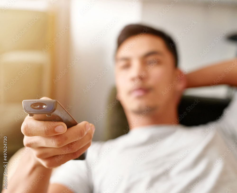 Seeking the sports channel. Shot of a young man using a remote control to change the channel on his 