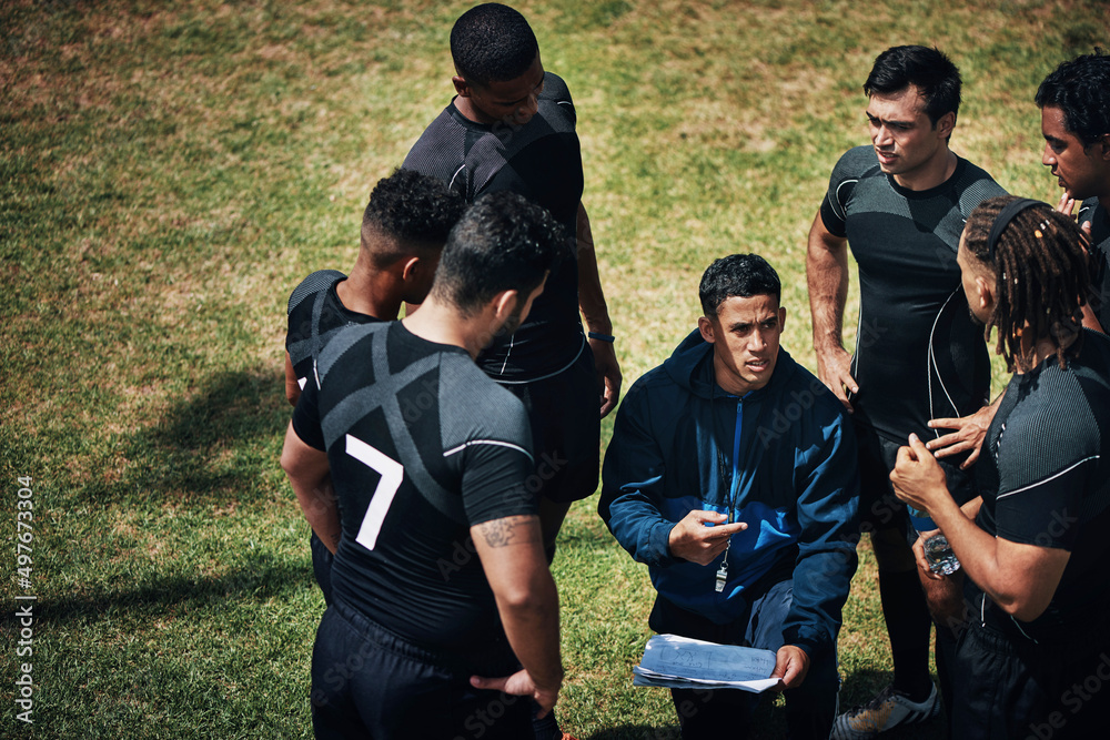 Is everyone here. Cropped shot of a handsome young rugby coach addressing his team on the field duri