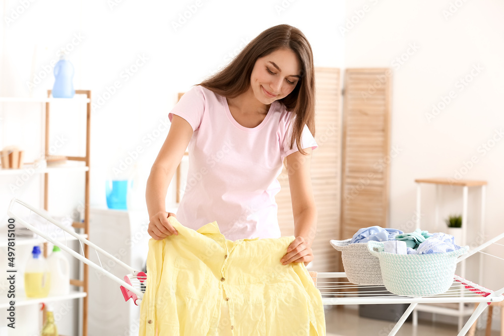 Beautiful housewife hanging clean clothes on dryer at home