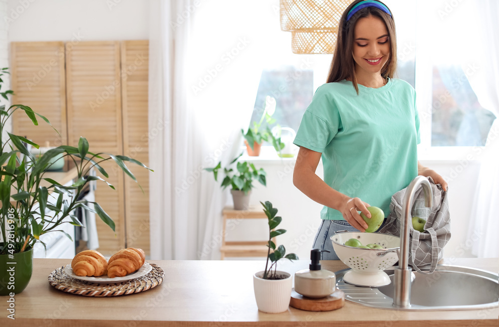 Young woman putting apple from eco bag into colander in kitchen