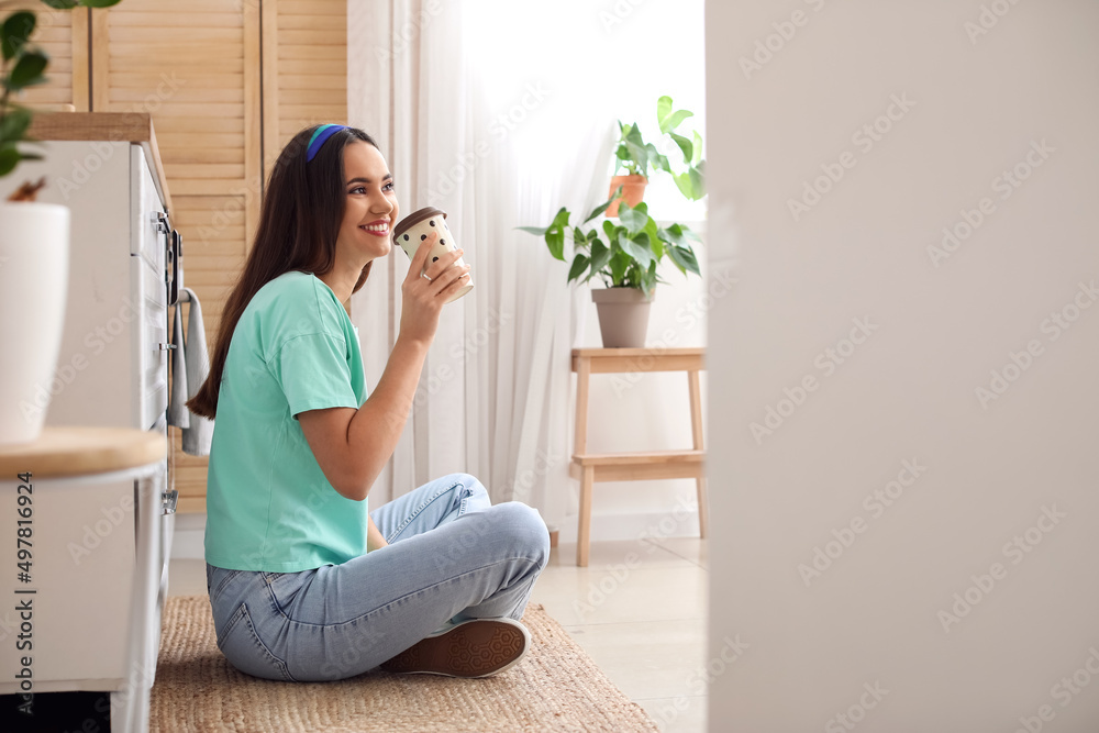 年轻女子在厨房地板上喝咖啡