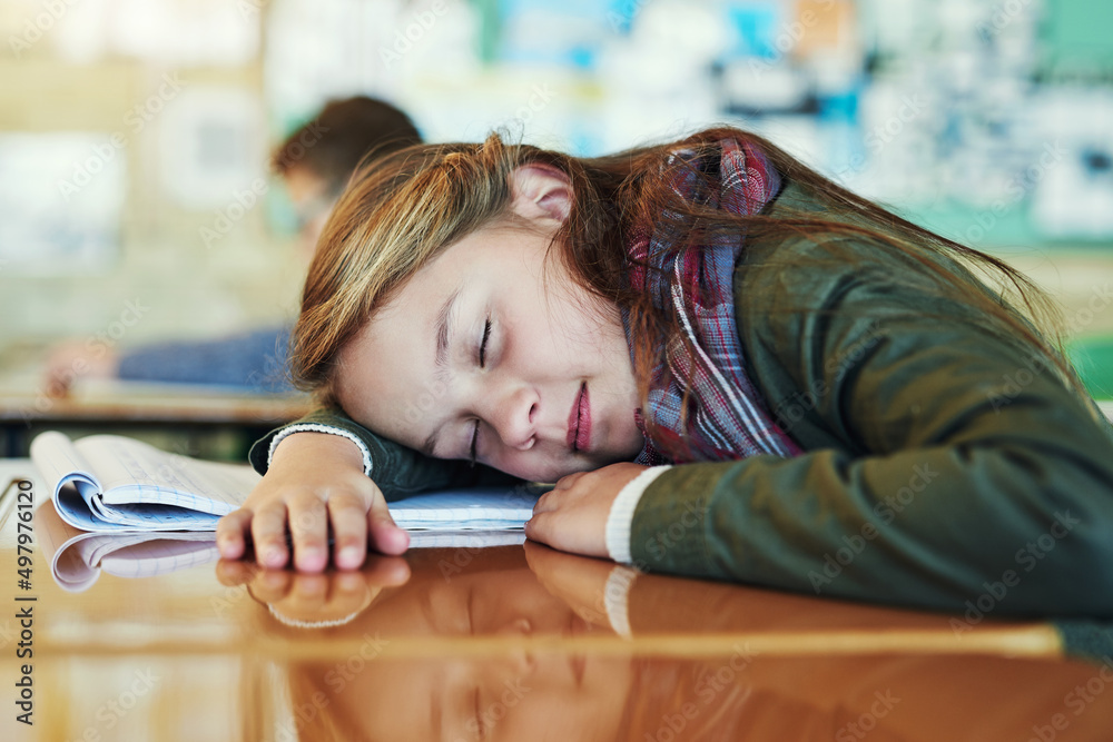 她正在刷新她年轻的头脑。一张可爱的小学女生在桌子上打盹的照片。i