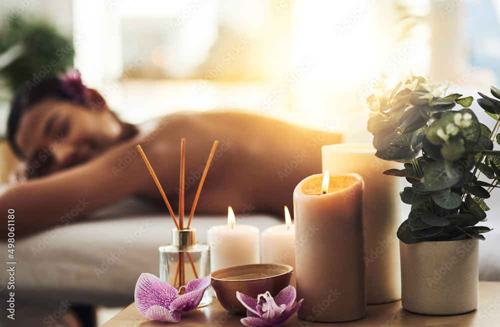 Indulge in a spa day. Shot of spa essentials on a table with a woman getting a massage in the backgr