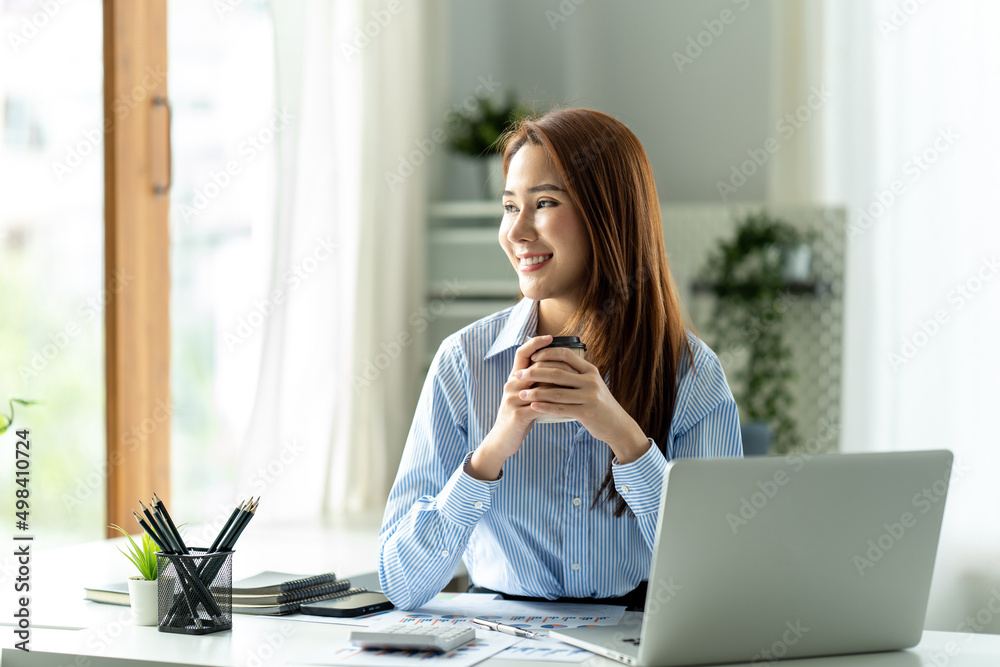 亚洲商务女孩在她的工作站上微笑着拿着咖啡杯。